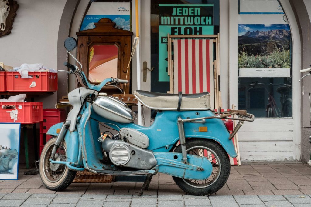 A somewhat battered blue vintage scooter in front of a secondhand store in Ramsau am Dachstein