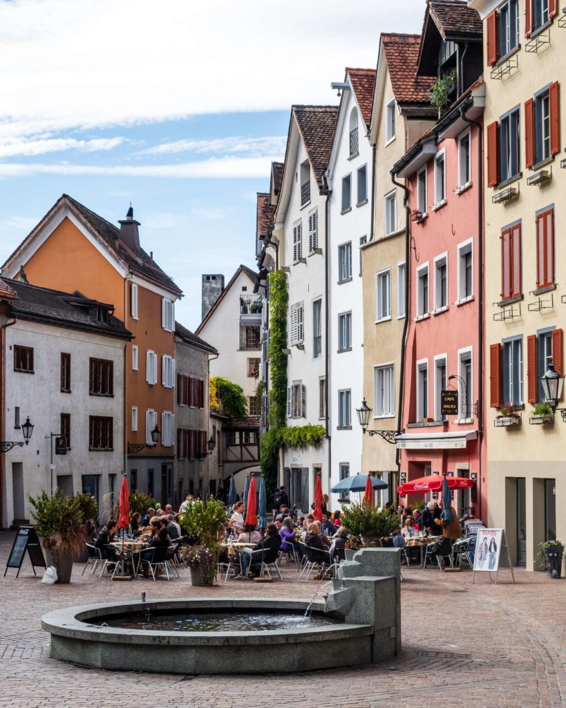 The town square of Chur with a small fountain and tall narrow medieval buildings