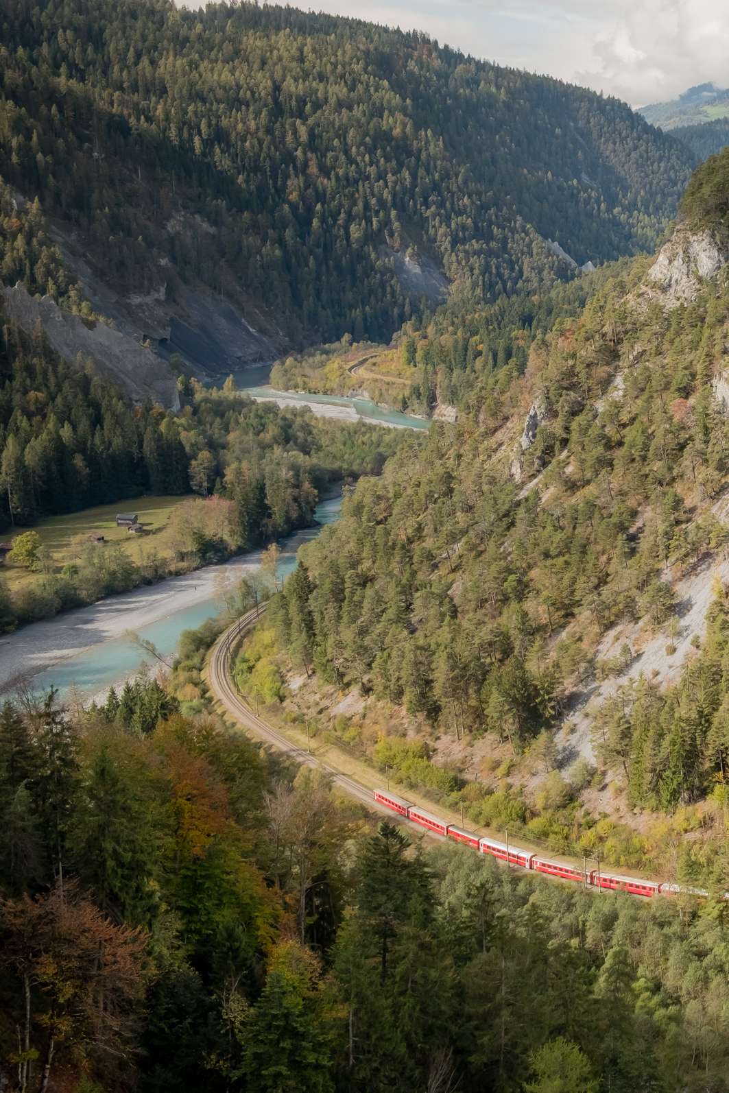 The Glacier Express train in the Grand Canyon of Switzerland, weaving through the valley next to the chalk coloured Rhine