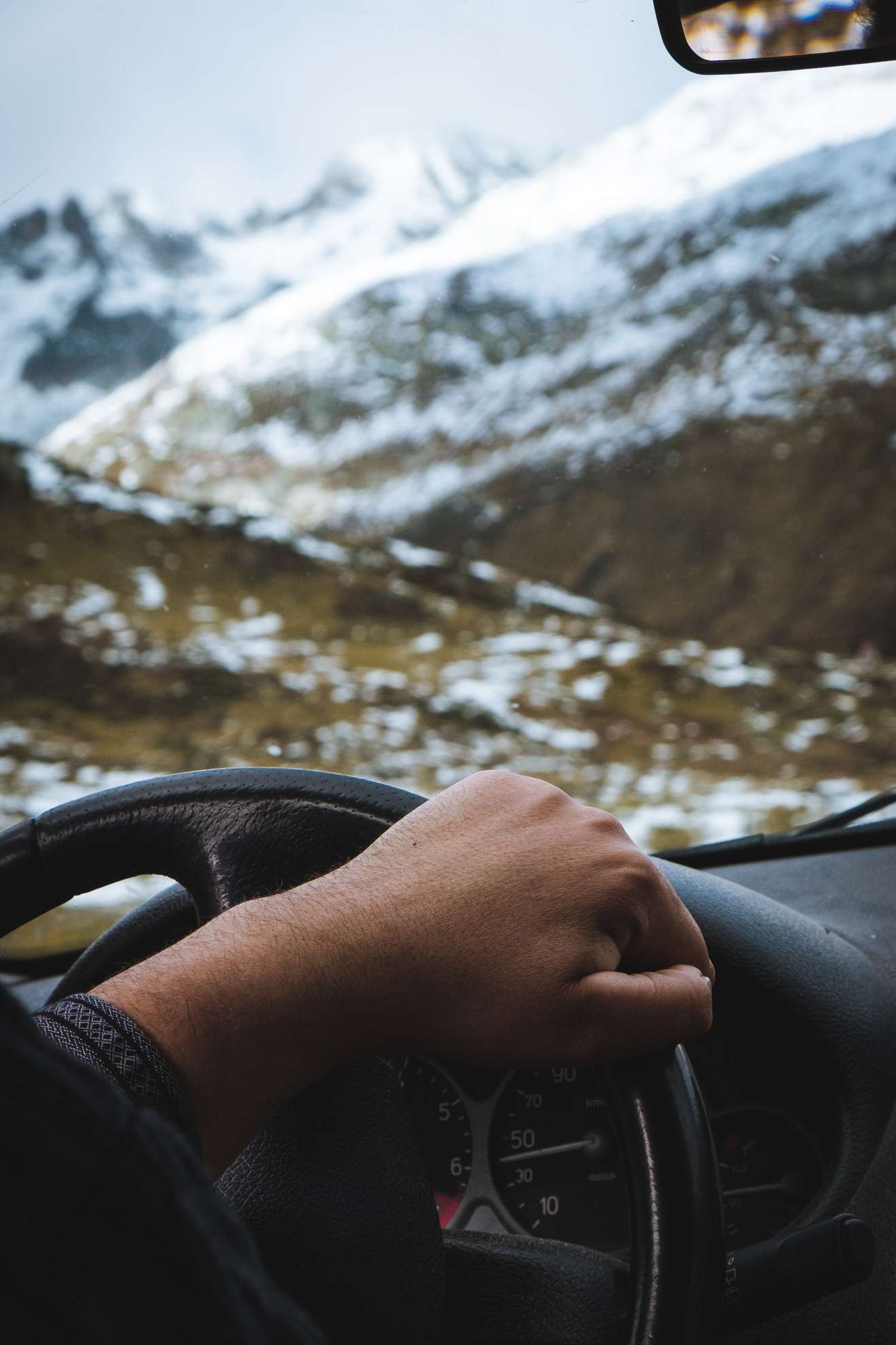Thomas's hand on the steering wheel as he drives us through the snowy, mountainous landscape of Switzerland in the back