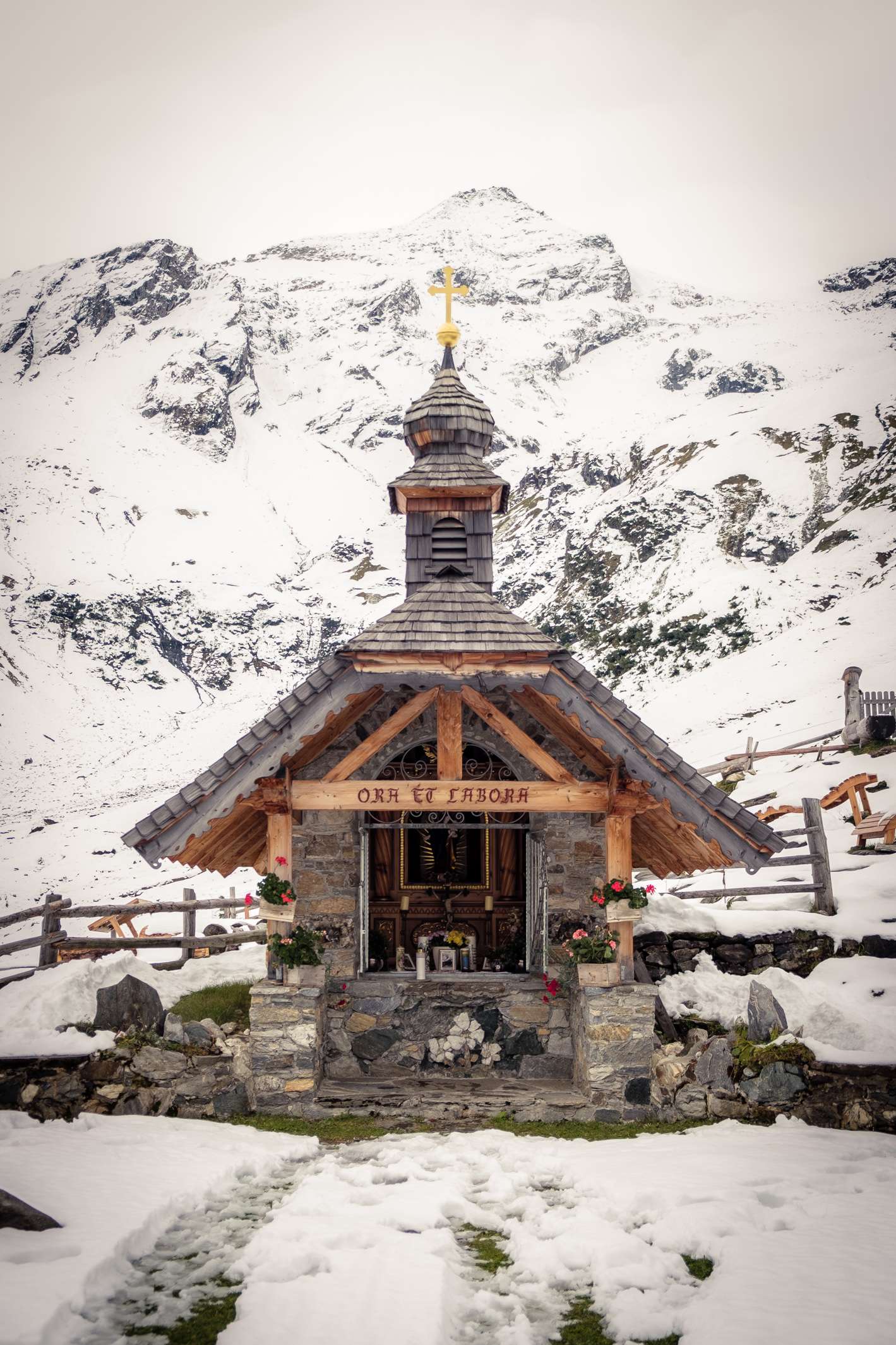 A small cute chapel made from wood and stone surrounded by snow at Stausee Mooserboden