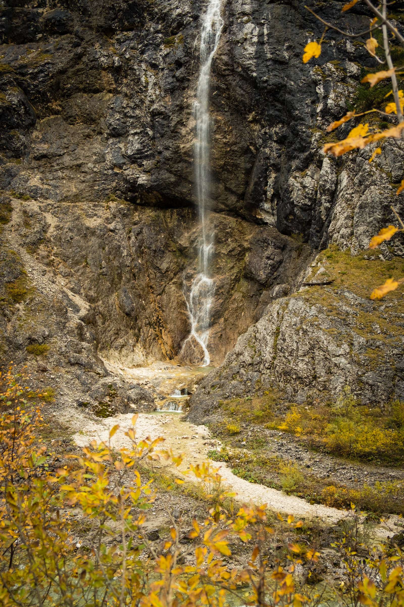 A tall thing waterfall framed by yellow autumn leaves