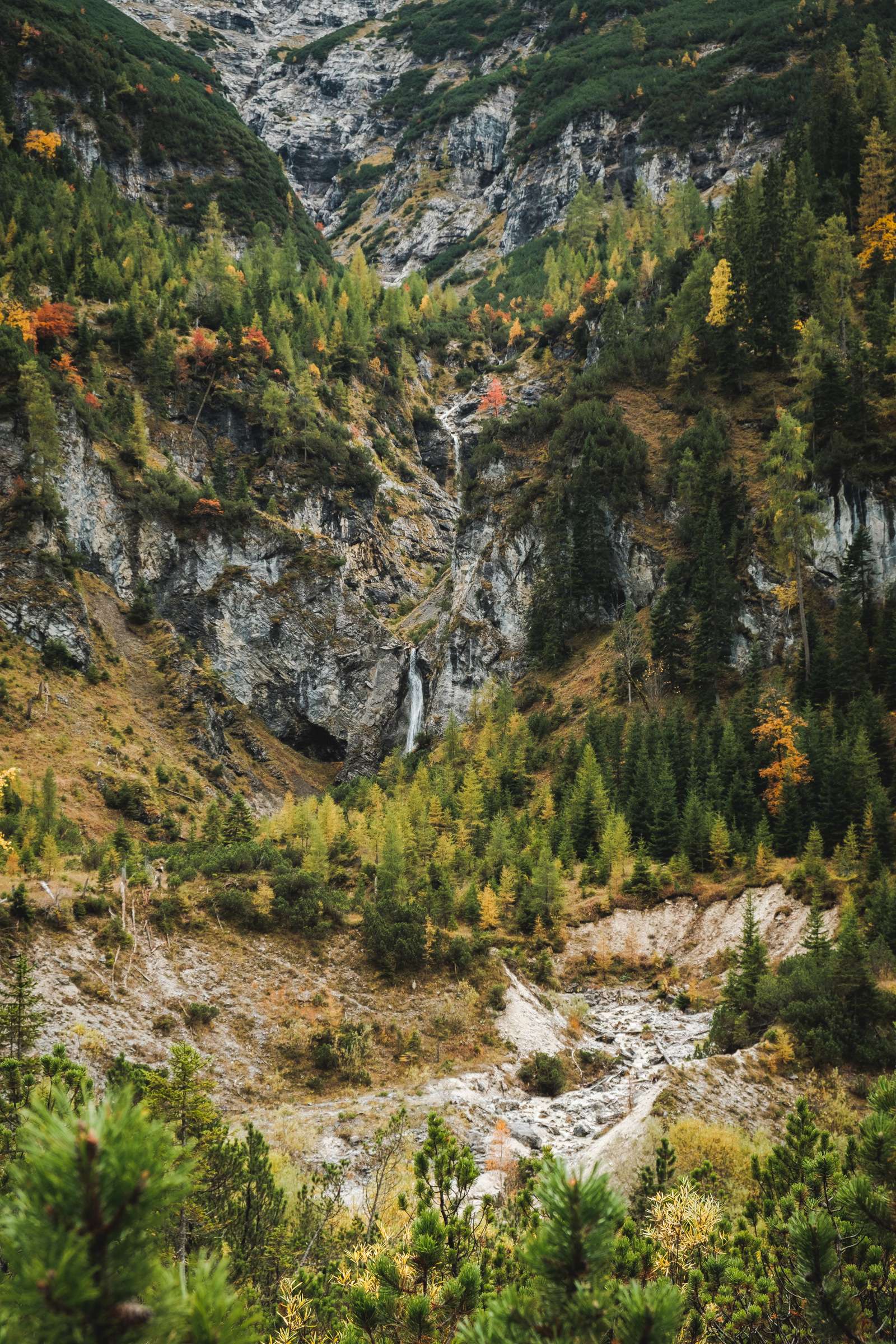 A magical waterfall scene in the Karwendel flowing over multiple levels of dense autumn forest