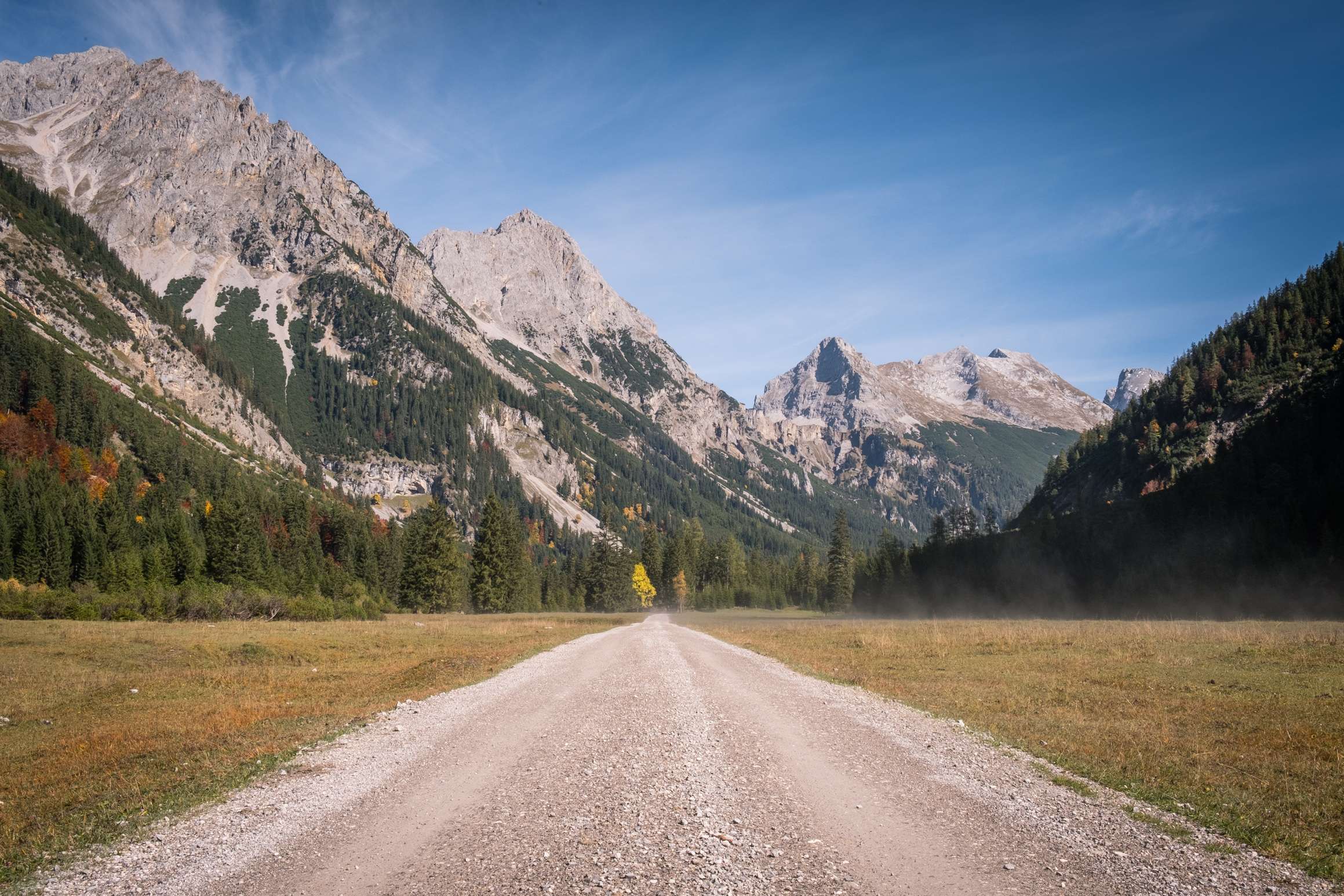 A dirt road running through an flat meadow in the Karwendel surrounded by massive mountains.