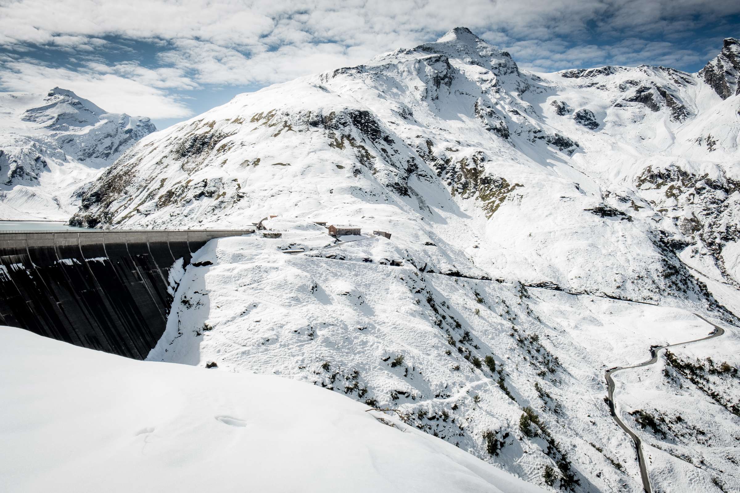 Winding road leading up to the higher damn wall of Mooserboden surrounded by snowy mountains