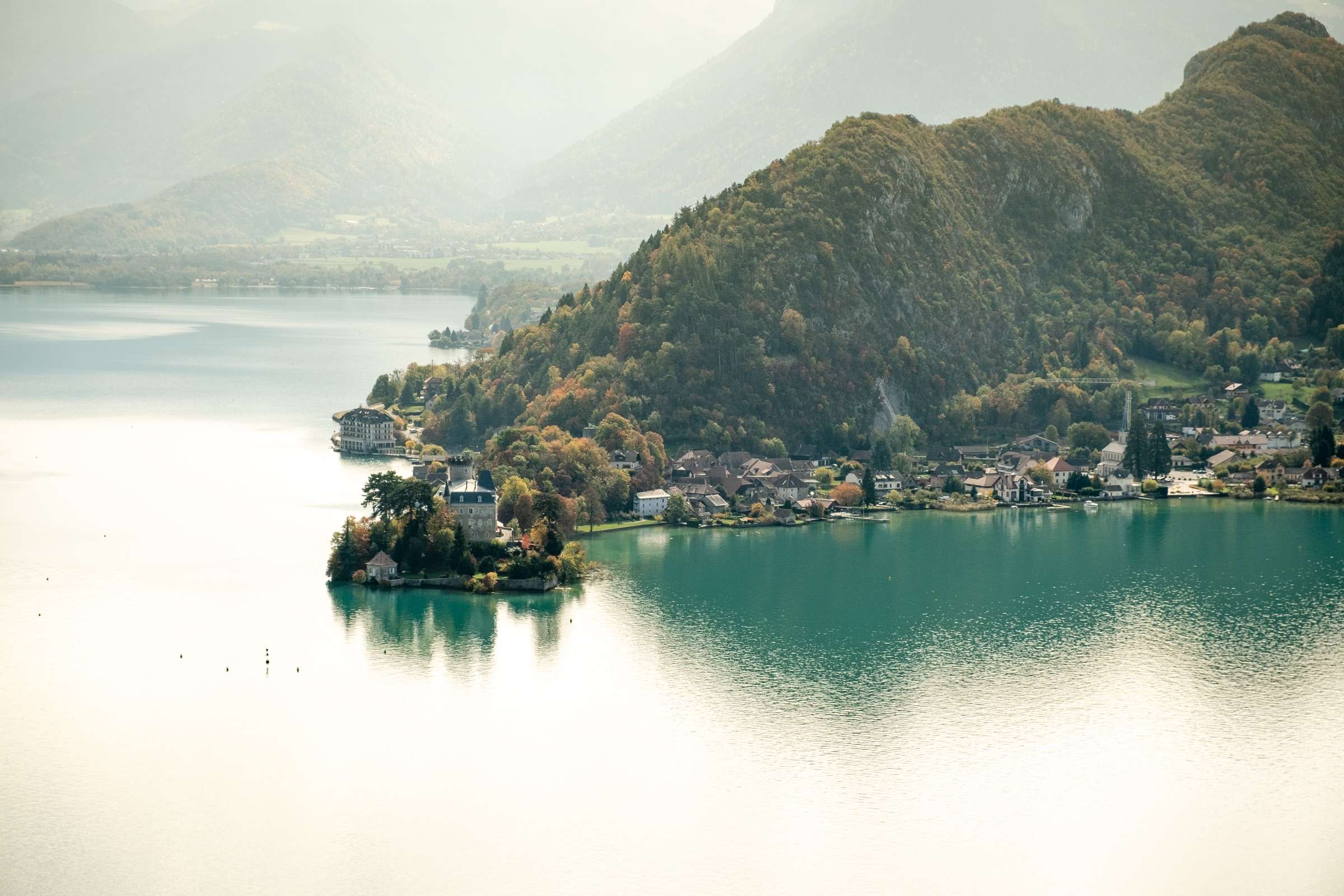 A manor on a peninsula to lake Annecy with mountains behind