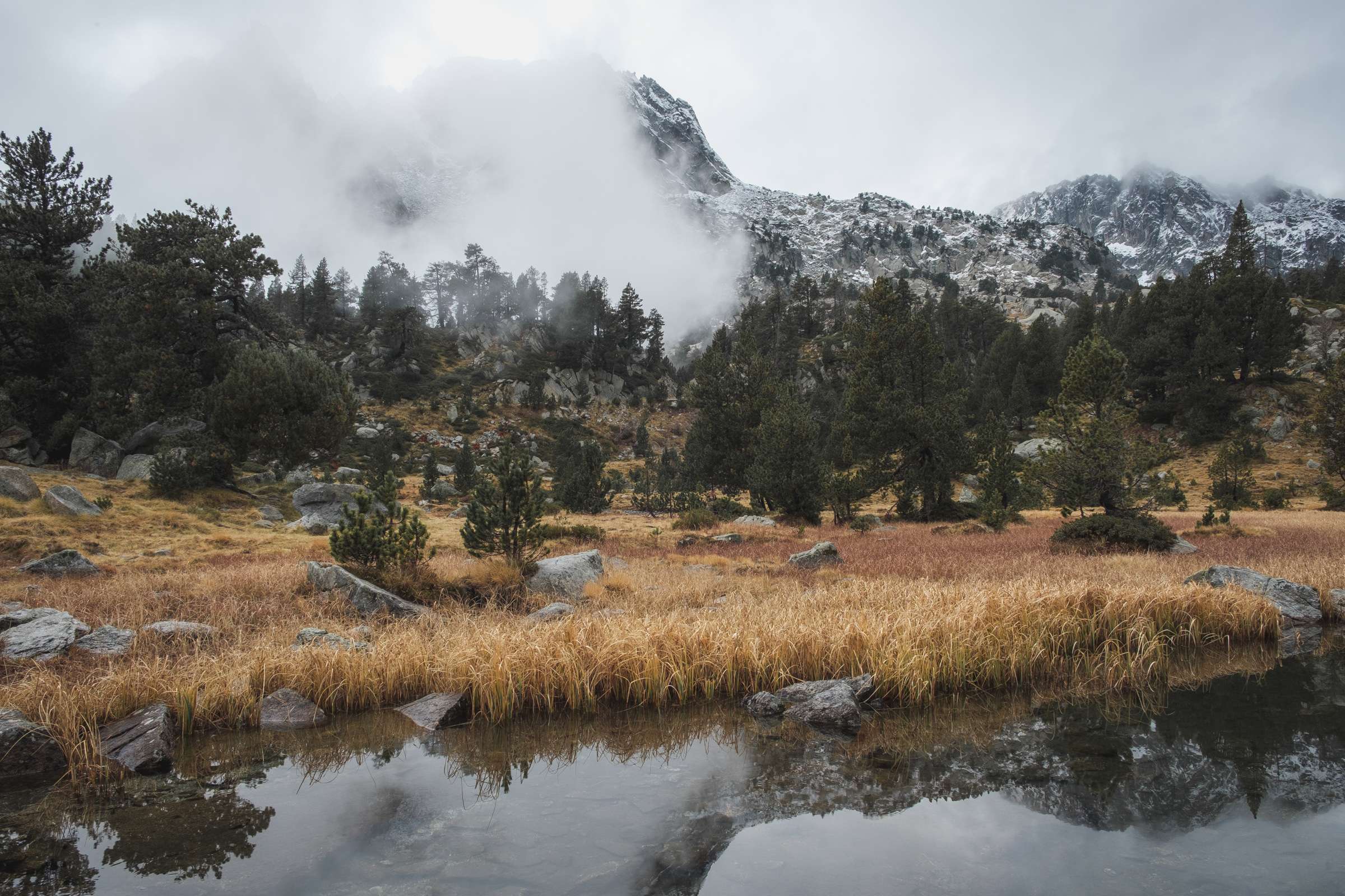 Still river mountain scene with meadows of orange grass