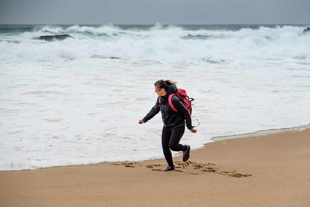 Caroline running from waves at Praia da Adraga beach