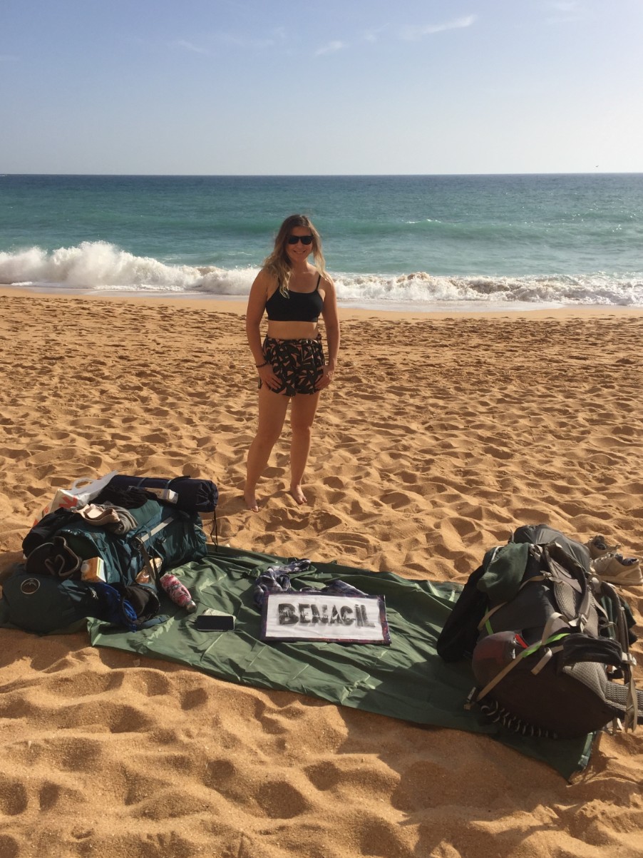Caroline standing proud on Benagil beach with hitchhiking sign and rucksacks