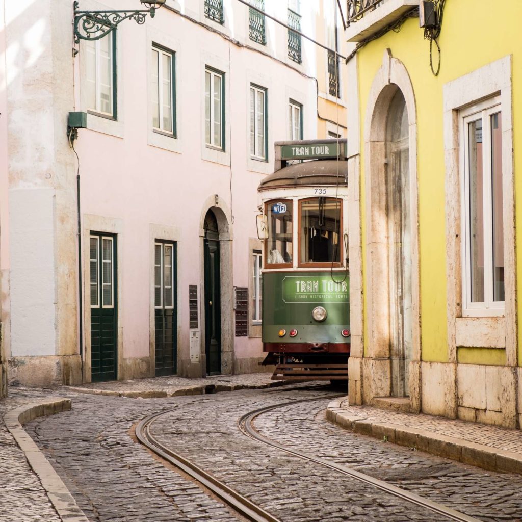 Cute green tram around a tight corner in Alfama, Lisbon