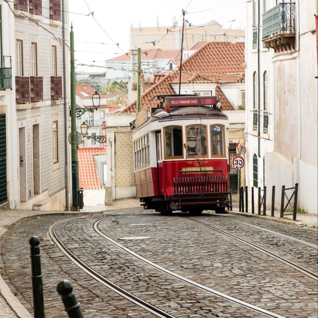 Cute red tram on cobbled street in Alfama, Lisbon