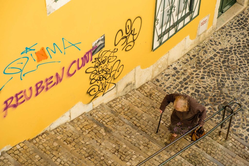 Old lady climbing cobbled staircase with graffiti on walls