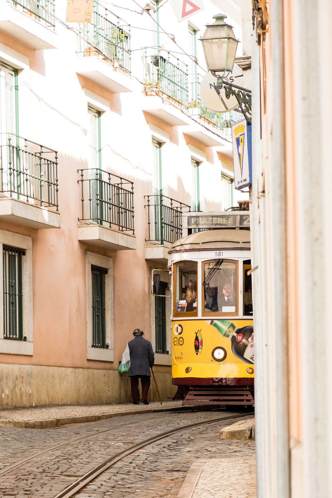 Yellow tram squeezing past old man in narrow cobbled street