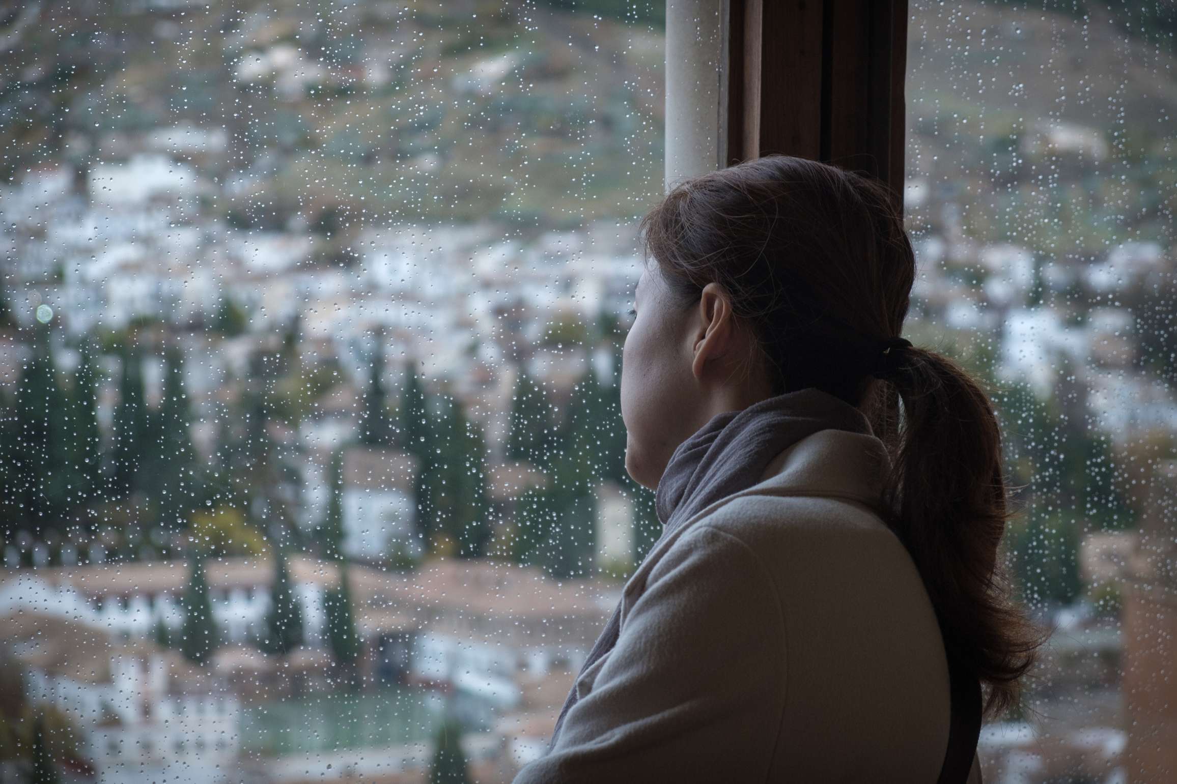 A woman looking over Granada through a rain covered window, The Alhrambra