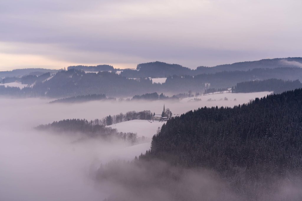 Layers of snow covered mountains and fog surrounding a church, Lavanttal, Carinthia