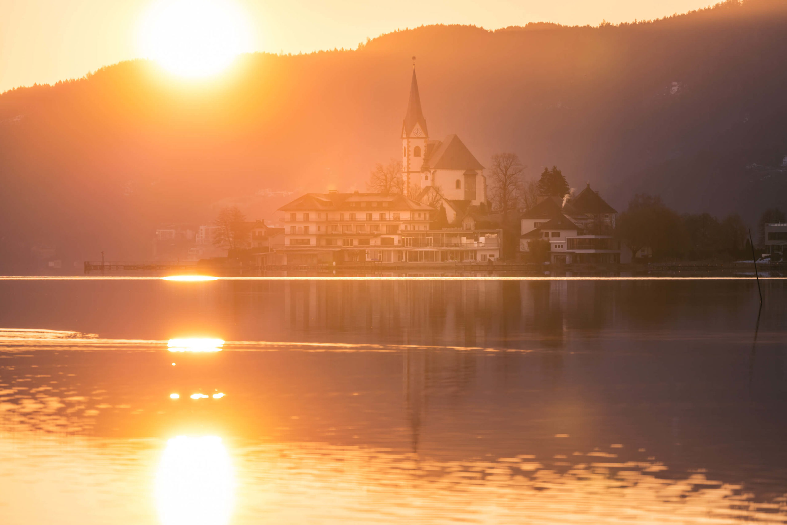 Golden morning sunrise over the pilgrim village and church of Maria Wörth on lake Wörthersee, Carinthia