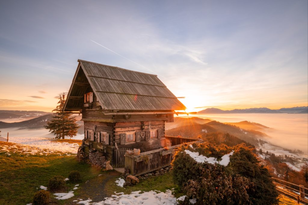 Magical warm winter sunrise over a cute mountain hut on Magdalensberg with thick fog covering Lower Carinthia