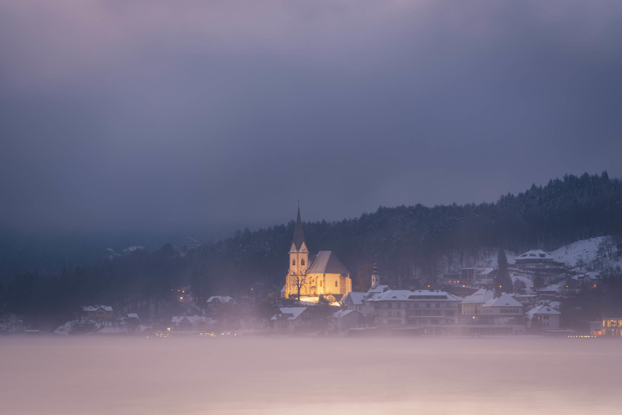 Thick cloud and fog on a turbulent morning at lake Wörthersee with illuminated church of Maria Wörth, Carinthia