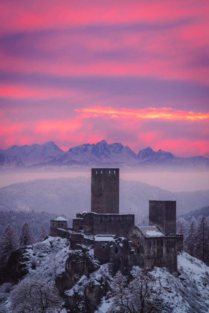 Vibrant pink sunset over snow covered Liebenfels castle with the mighty Karawanken mountains looming above, Waggendorf, Carinthia, Austria