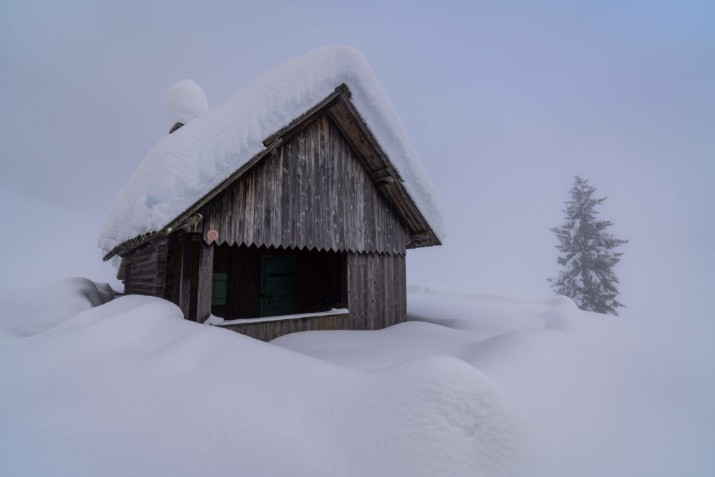 Wooden cabin covered in thick layer of snow surrounded by fog in the winter, Zell Pfarre, Carinthia