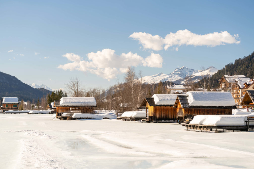 Wooden huts with lots of snow on top and snowy mountains in the background, Weissensee, Carinthia