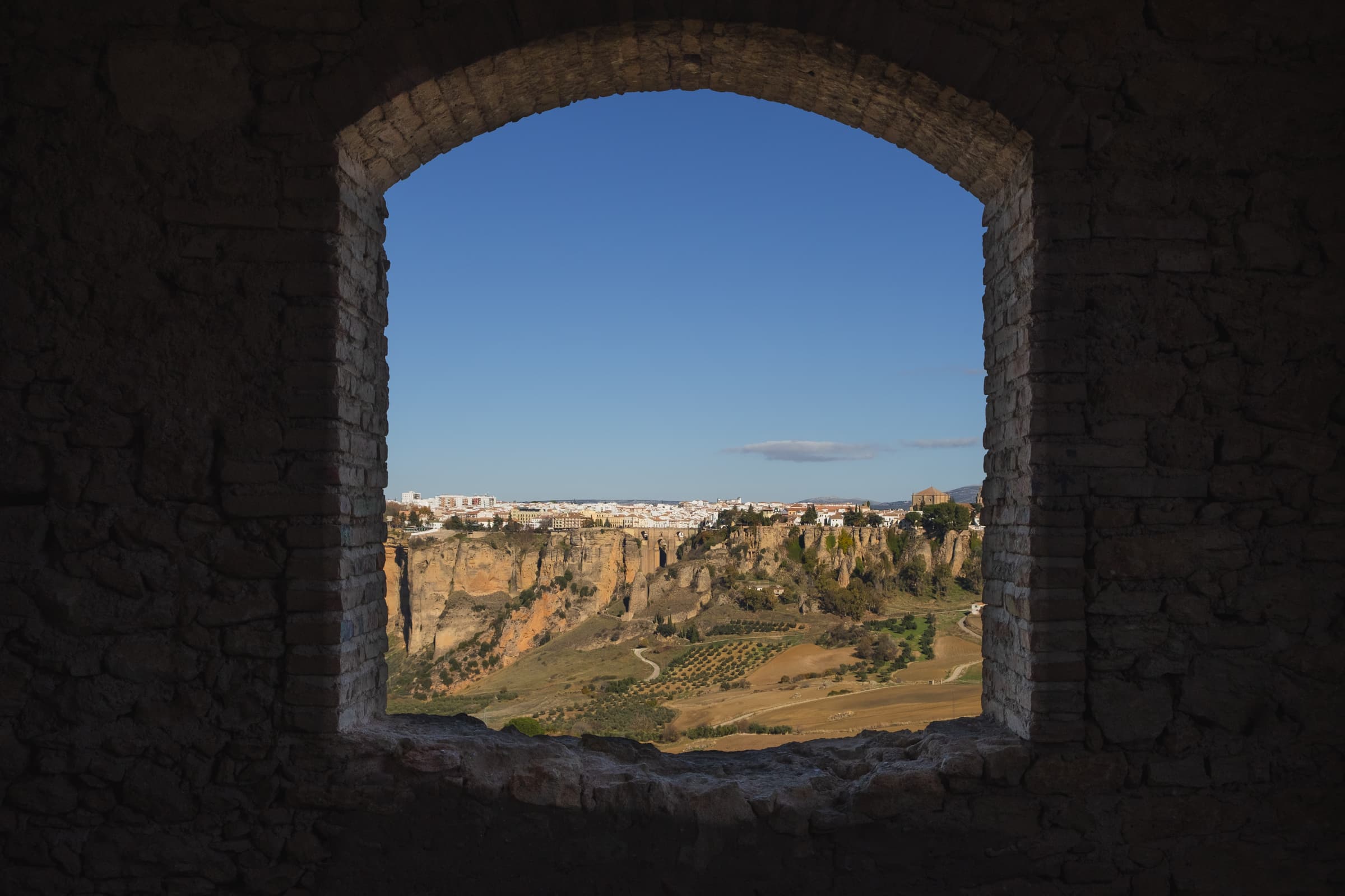Ronda on a sunny day through the window of an abandoned building, across the valley, Spain