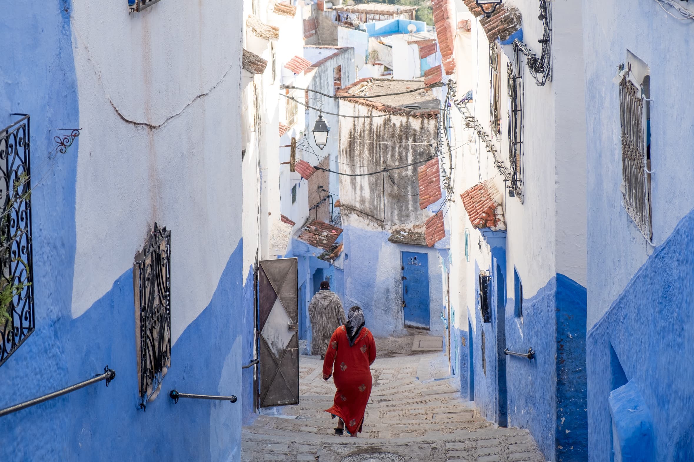 A woman in a red dress hurrying down a side street, Chefchaouen, Morocco