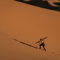 Caroline climbing a sand dune with a snow board