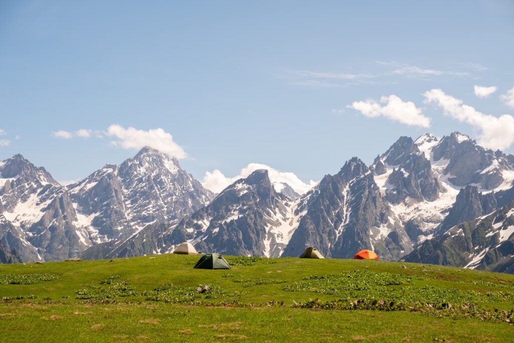 Tents on a green meadow with blue skies and jagged snowy peaks in the background