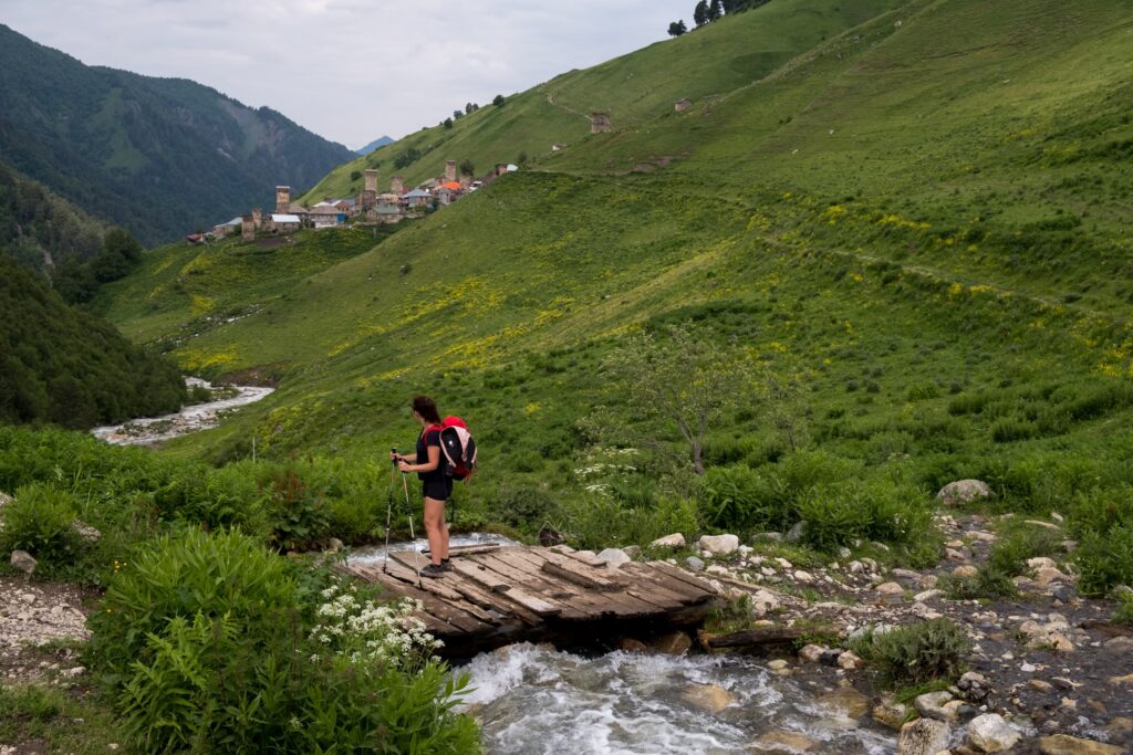 Caroline crossing a stream looking back to Adishi on a gloomy morning