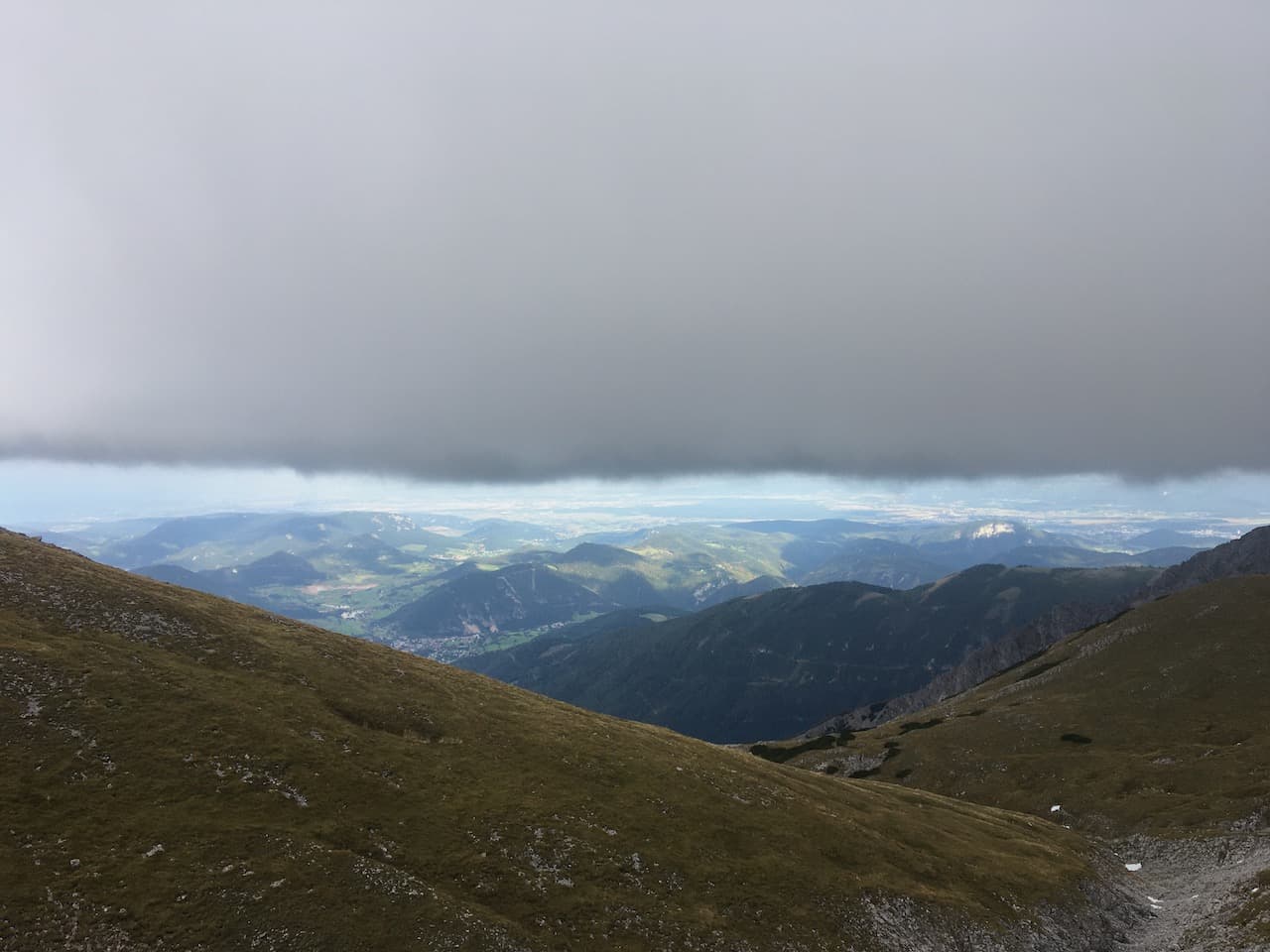 A wall of clouds coming down in a straight horizontal line, stopping shortly before the panoramic view onto the Viennese Hausberge from near the top of Schneeberg