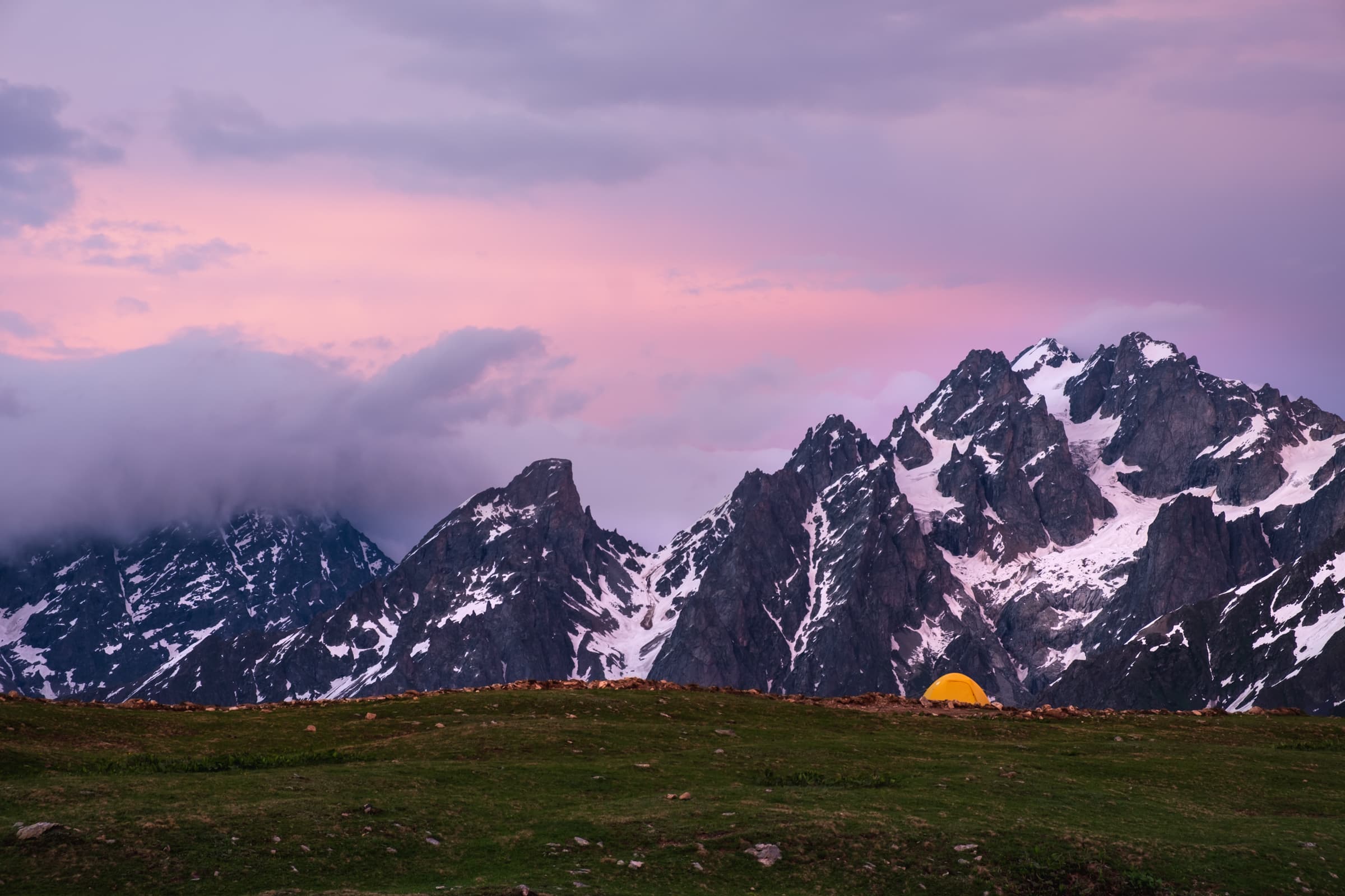 Pink and purple sky after a burning sunset at Koruldi lakes with cosy glowing tent, high in the Caucasus mountains of Svaneti, Georgia