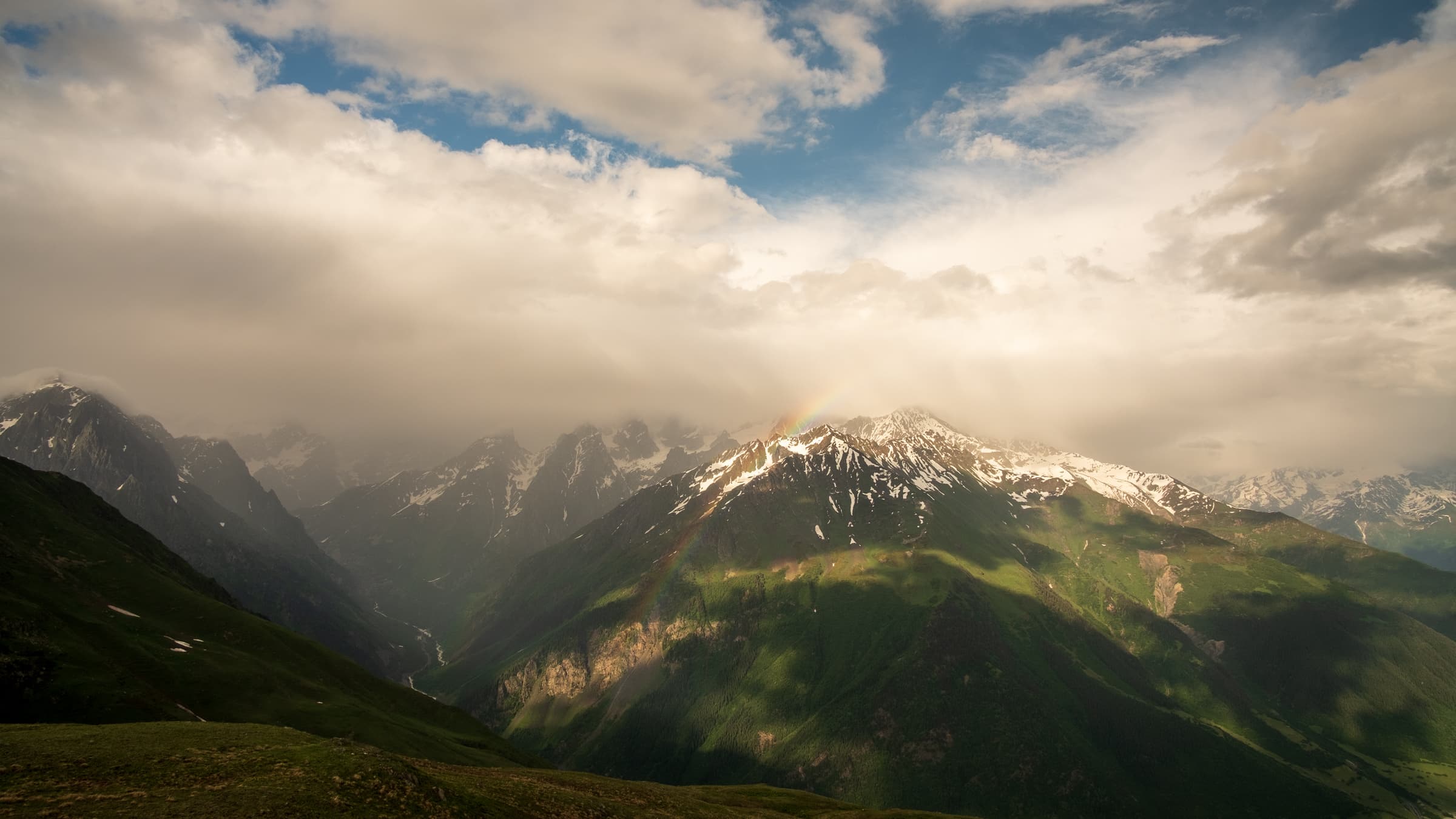 Storm brewing in the Caucasus mountains with a rainbow piercing through the clouds