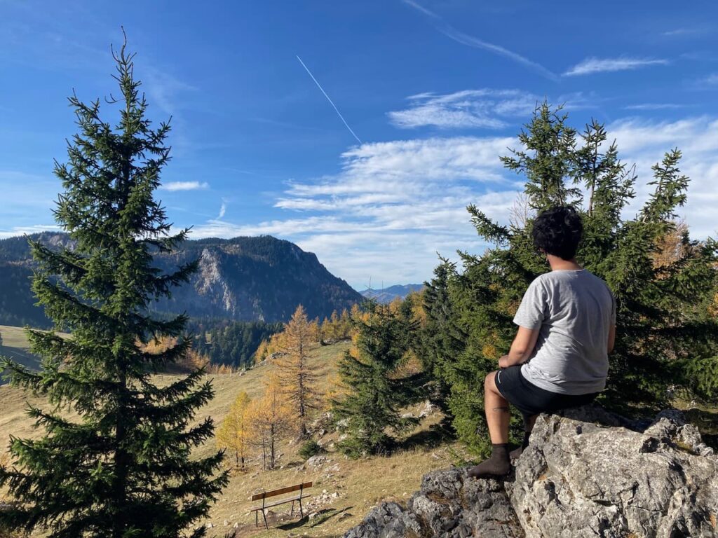Aydin sitting in the sun on a rock in a meadow while taking a break on Schneeberg in the midst of autumn colours