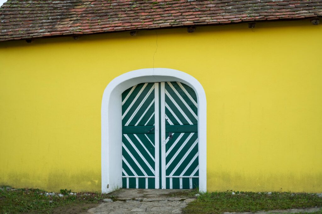 Bright yellow wine cellar building with diagonal-striped green decorative door in Zellerndorf (Maulavern) Kellergasse