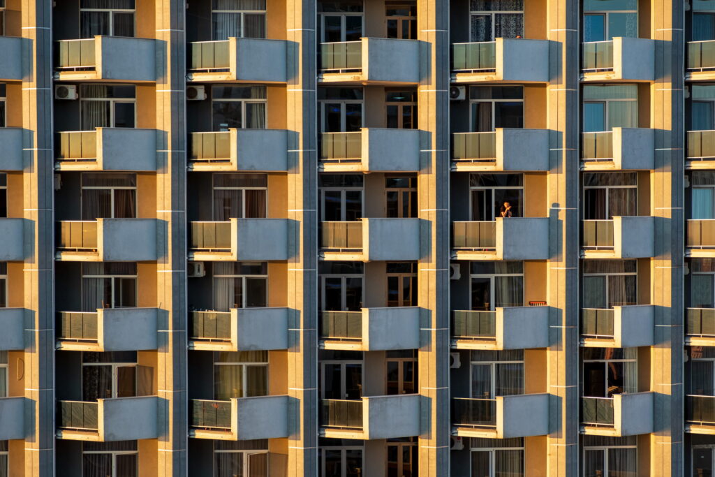 Golden sun illuminating an apartment block with repeated balconies and one single smoking man in Batumi