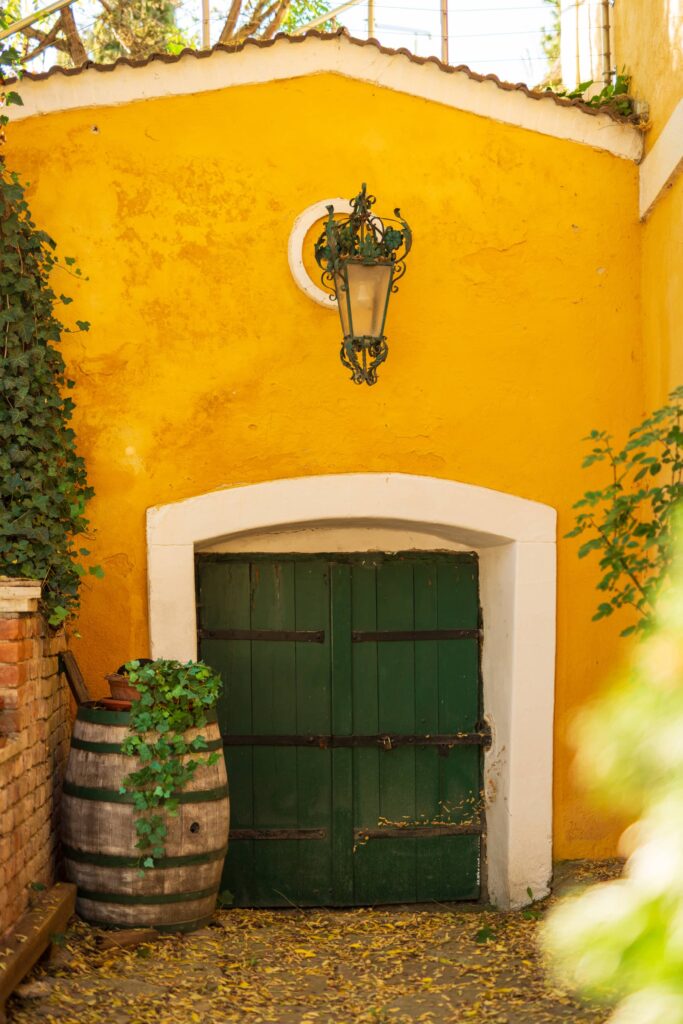 Entrance to a yellow wine cellar building with green wooden door and lantern decorated with leaves at Große Kellertrift, Haugsdrof