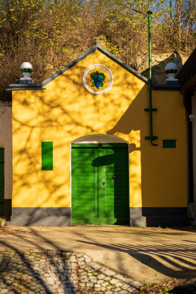 Bright yellow and green wine cellar with decorative 3D ceramic house emblem shaped like a wine leave at Große Kellertrift, Haugsdorf