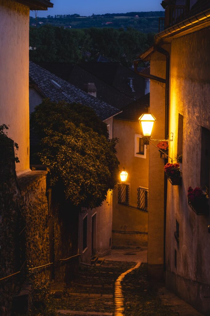 Narrow cobbled path between medieval buildings leading down to the Danube lit up with traditional streetlamp in Stein