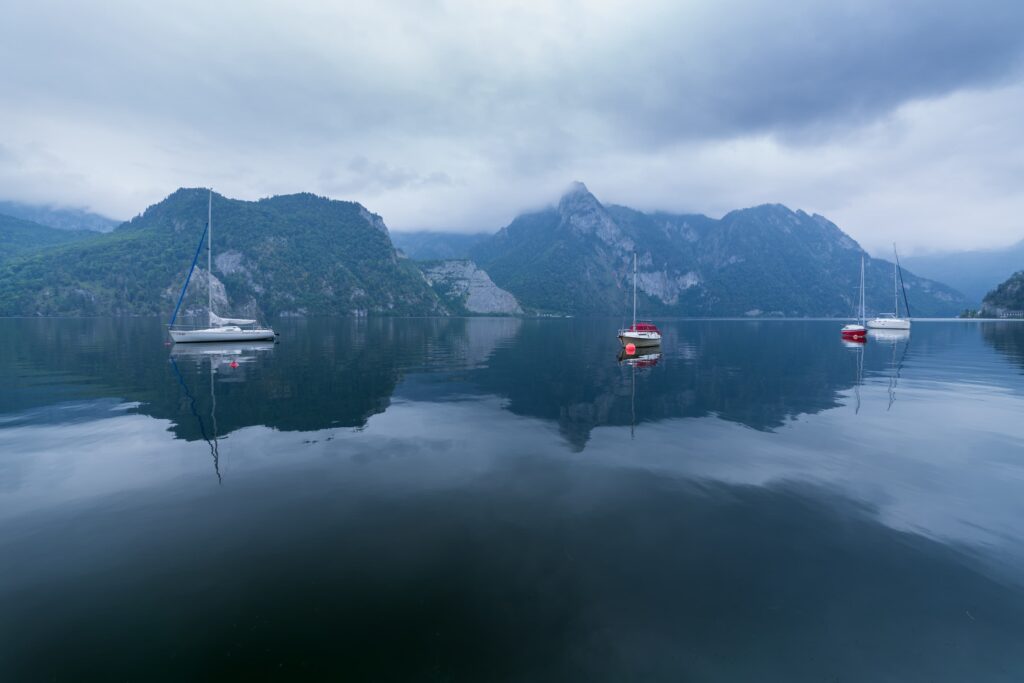 Calm overcast day looking over lake Traunsee, with still moored boats on lake and foreboding mountains rising in the clouds